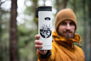 Sea to Sky Sticker on a white insulated travel mug in a forest setting, showcasing outdoor design by a Canadian artist.