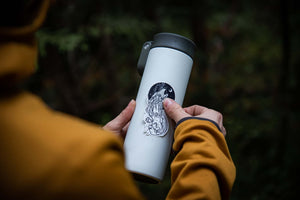Person holding a white travel mug featuring a Sea Wolf Sticker outdoors, showcasing original black and white illustration.