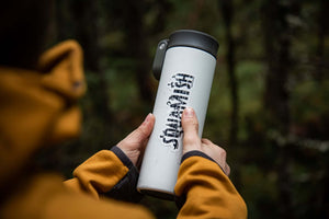 Squamish Sticker on a white travel mug held outdoors, showcasing original illustration by a Canadian artist.
