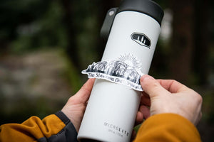 The Stawamus Chief Sticker applied on a white travel mug, showcasing its glossy black and white design.