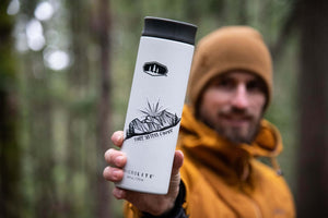 Three Sisters Mountain Sticker on a travel mug held by an outdoor enthusiast in a forest.