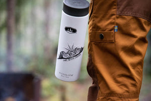 Three Sisters Mountain Sticker on a white water bottle held by a person wearing brown pants, outdoors.