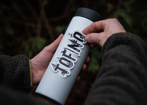 Person applying Tofino Sticker on a stainless steel tumbler, showcasing outdoor sticker design.