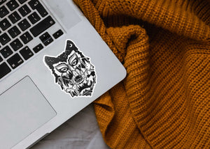 Wolf Head Sticker on a laptop beside a cozy knitted blanket, showcasing an original black and white illustration.