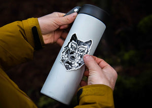 Wolf Head Sticker on a gray travel mug, showcasing black and white original illustration for outdoor use.