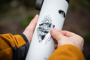 Person applying a black and white Yoho National Park Sticker on a stainless steel water bottle.