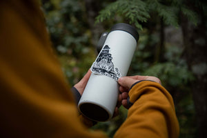 Yukon Sticker on a white thermal tumbler in an outdoor setting with trees, showcasing an original illustration by a Canadian artist.